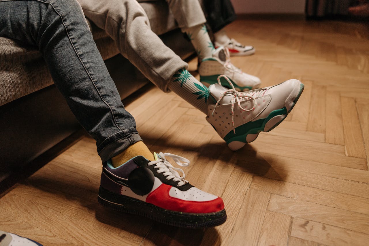 Close-up of legs in colorful sneakers relaxing indoors on wooden floor.